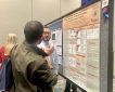 A researcher presents a scientific poster titled “Single-Nucleus RNA Sequencing Reveals the Immunological Microenvironment of HPV+ and HPV- Penile Cancer” to an attendee at a conference. The presenter explains findings while gesturing toward detailed charts and data, with a blue ribbon indicating a recognized poster.